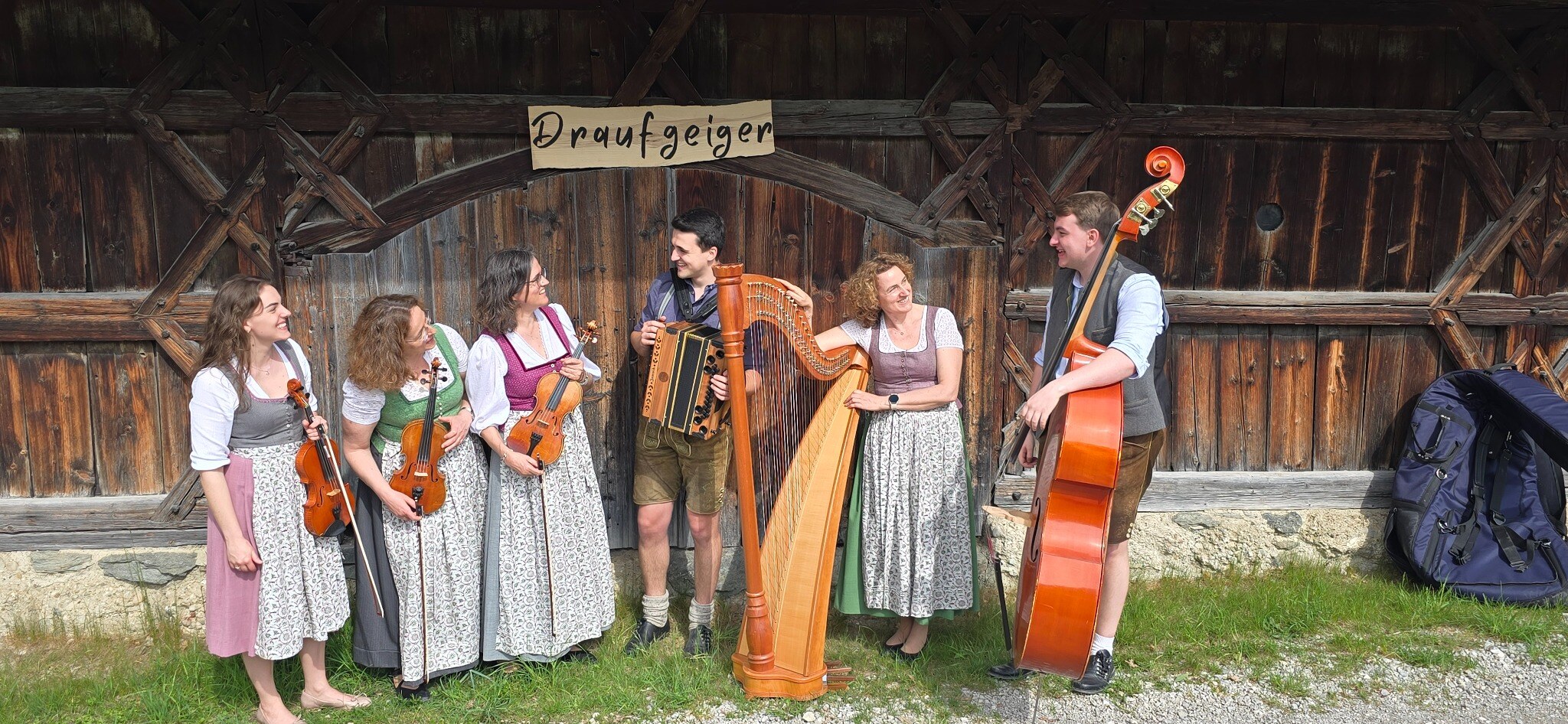 Die Draufgeiger mit Geigen, Ziach, Kontrabass und Harfe vor einem alten Holzstadl
